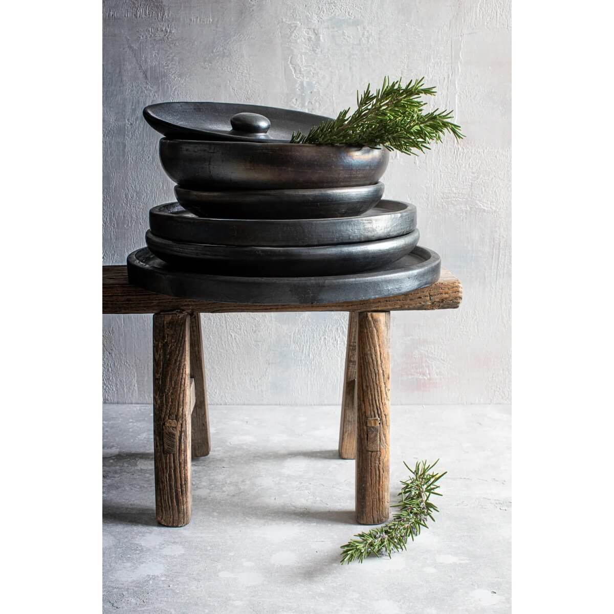 Bohemian style burned deep plate set in black terracotta, crafted by Bazar Bizar Living, stylishly stacked on a rustic wooden table.