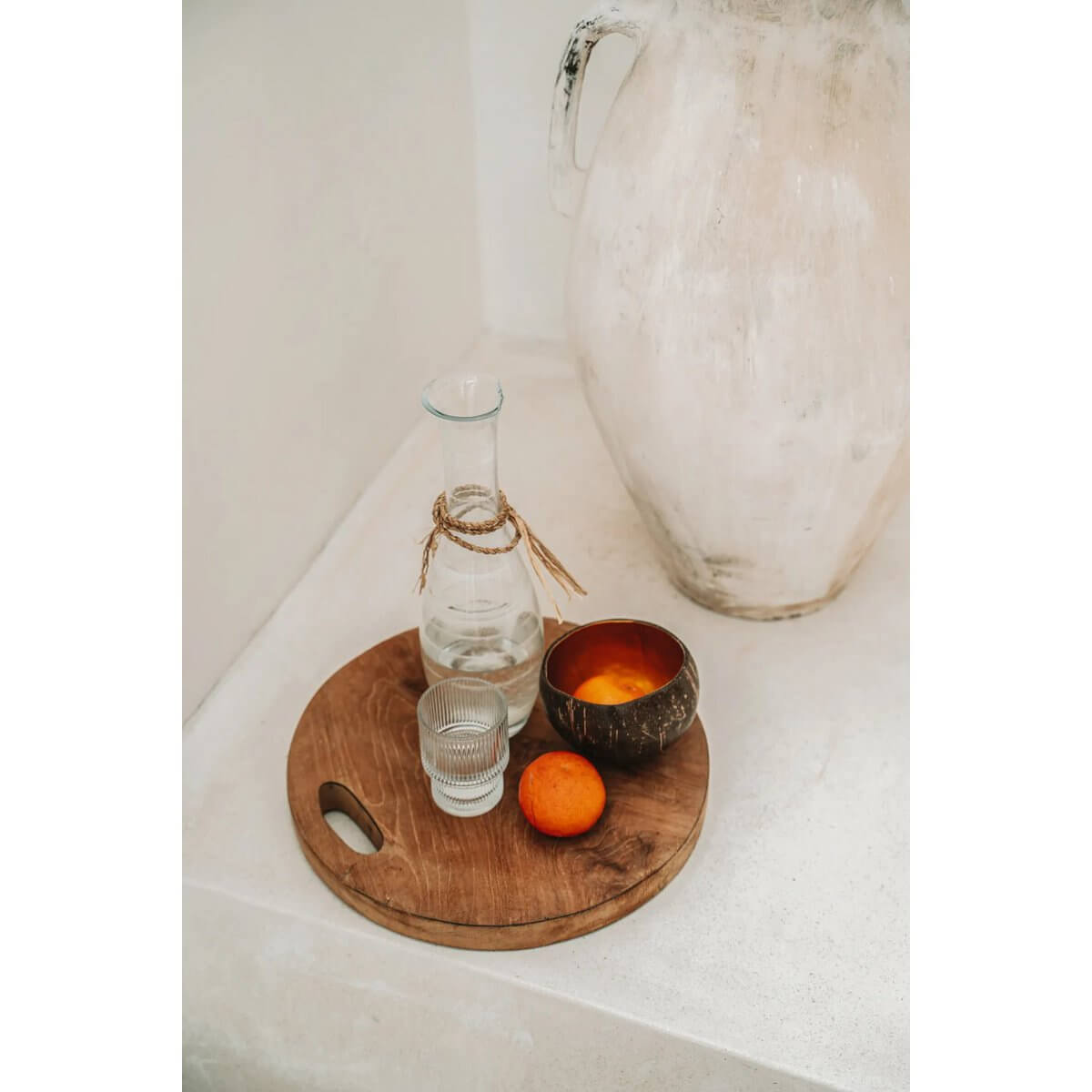 Bohemian style display with natural coconut food bowl, glass carafe, and fresh orange on a rustic wooden tray.