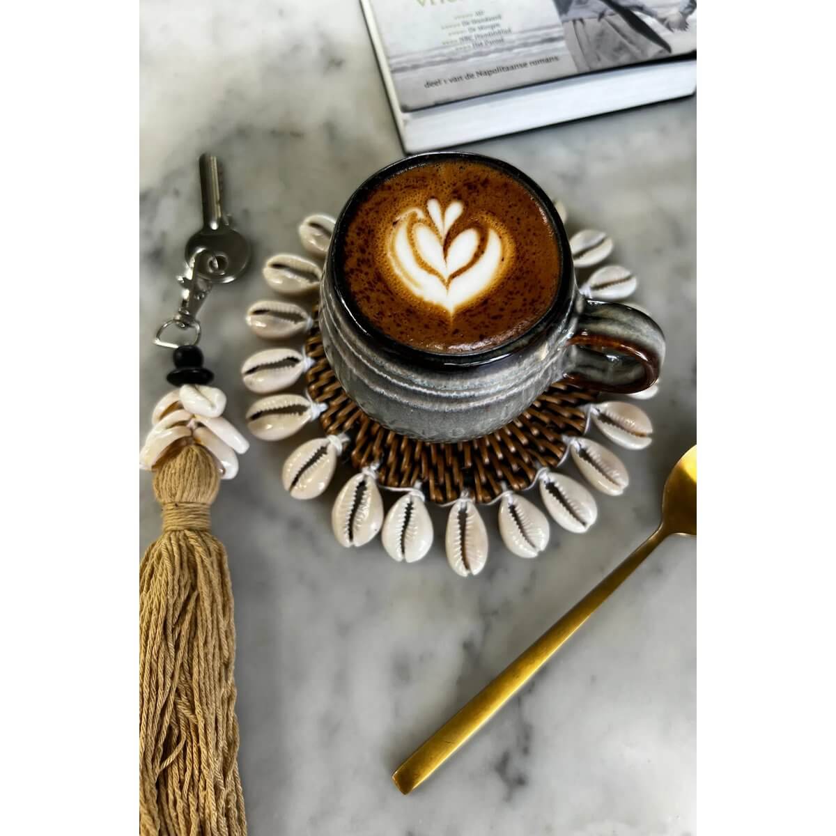 Bohemian coffee scene with latte on The Colonial Shell Coaster, featuring handwoven rattan and shell design on marble table.