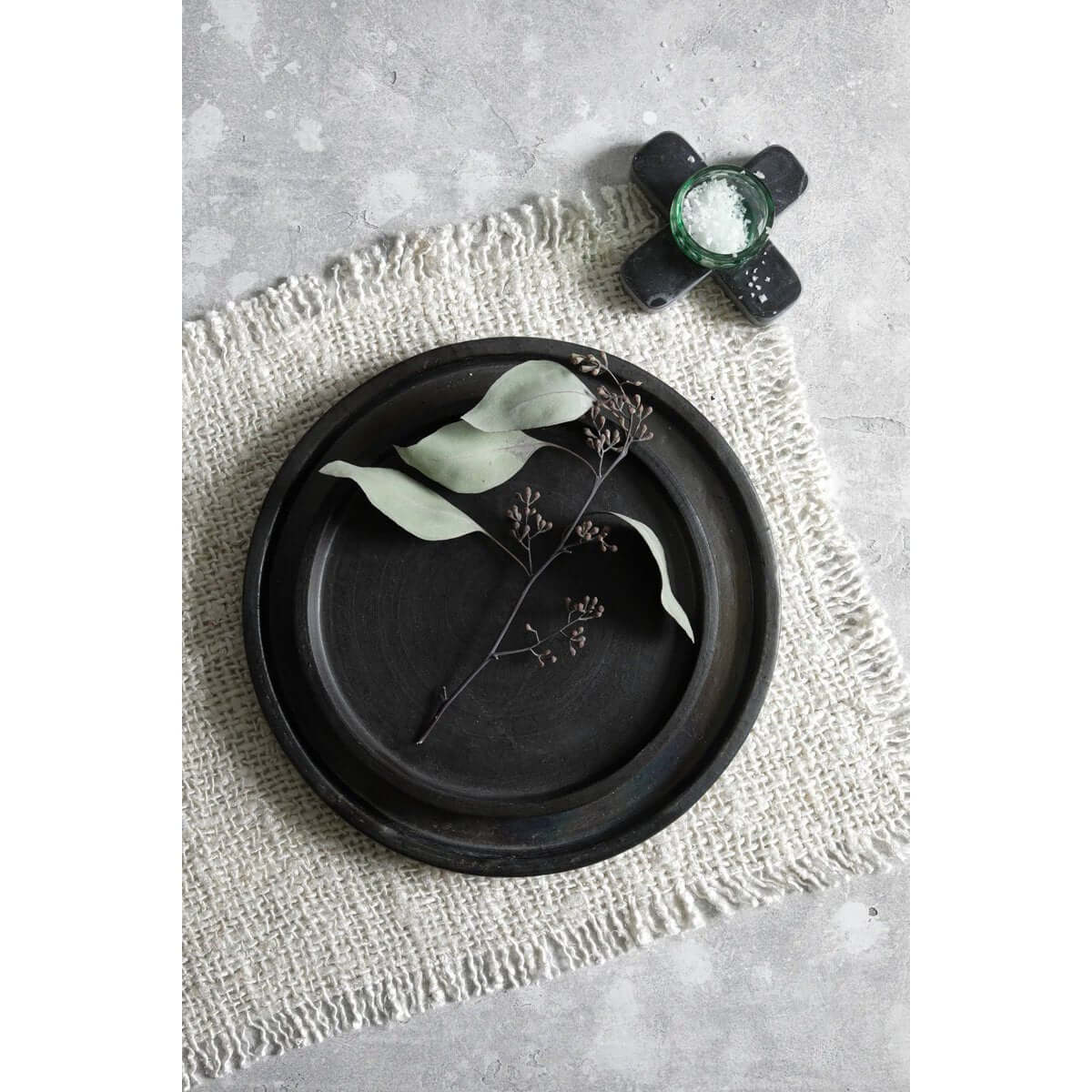 Crème katoenen placemat met wafelstructuur en luxe zijdelook, gedecoreerd met zwart keramiek en een groen blad, sfeervolle tafelsetting.