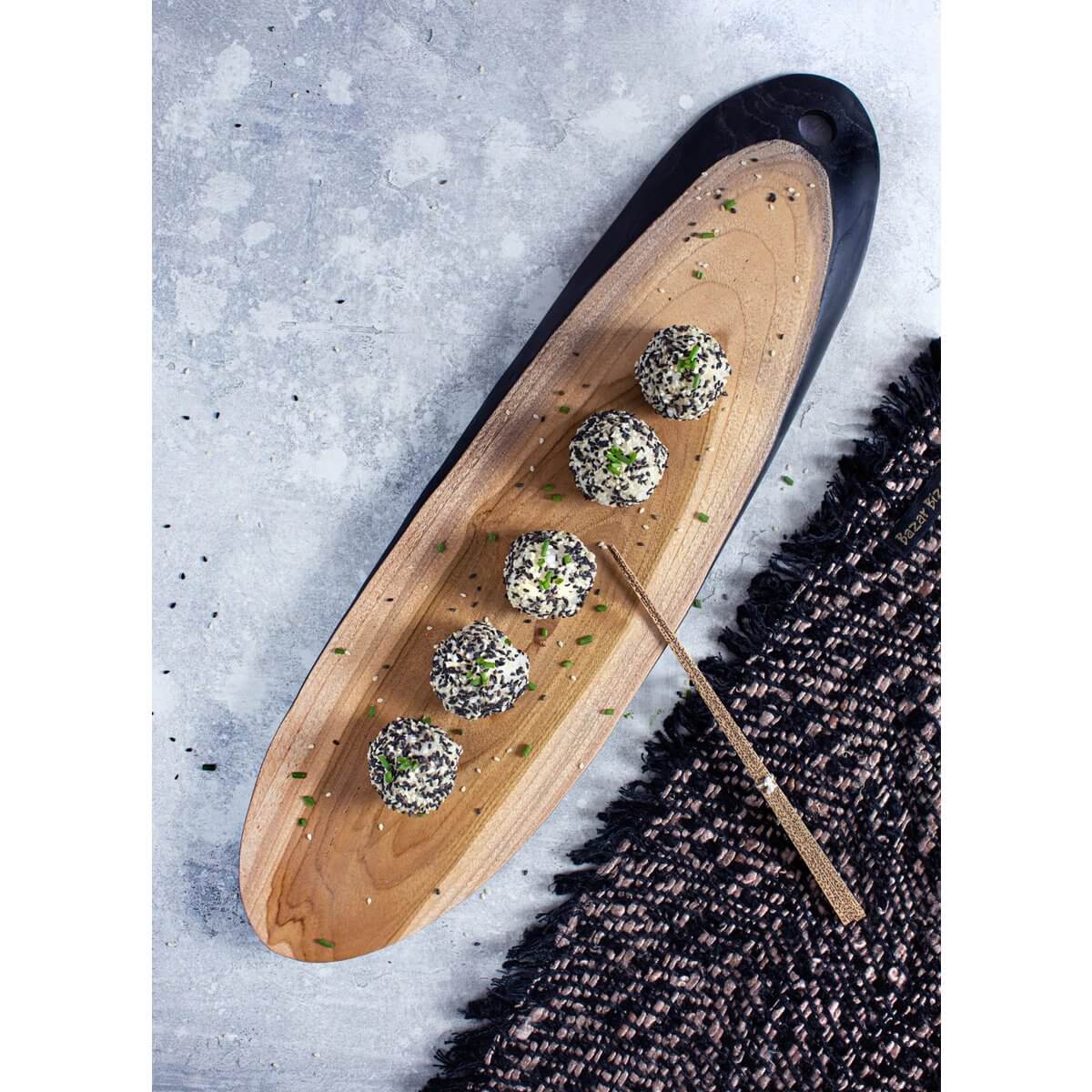 Houten plank met vijf gekruide kaasballetjes en een gouden vork op marmeren achtergrond en textiele ondergrond.