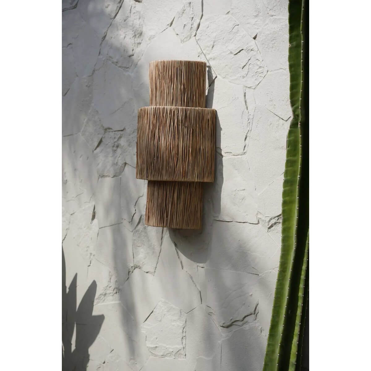 De Ohana wandapplicatie van natuurlijk materiaal, met unieke textuur en bohemien stijl, tegen witte muur geaccentueerd.