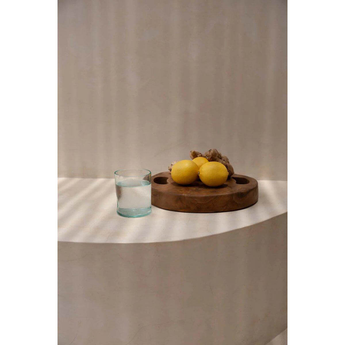 Teakhouten dienblad met citroenen en een glas water op een lichtgekleurd aanrechtblad, perfecte keukenaccessoire.