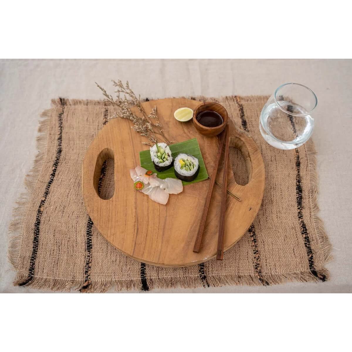 Ronde teakhouten snijplank dienblad met sushi op rustieke jute placemat, ideaal voor stijlvol serveren; Bazar Bizar Living.