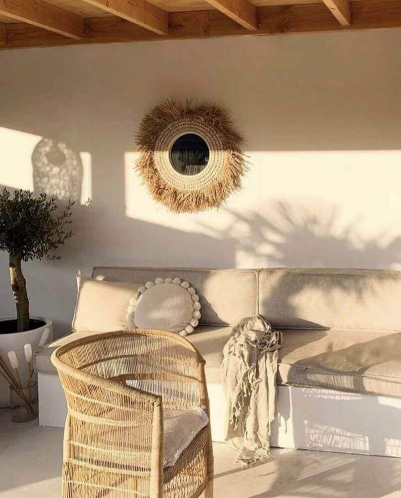 Boho spiegel met raffia en schelpen als blikvanger aan de muur in een lichte, bohemien woonkamer met rotan meubels.