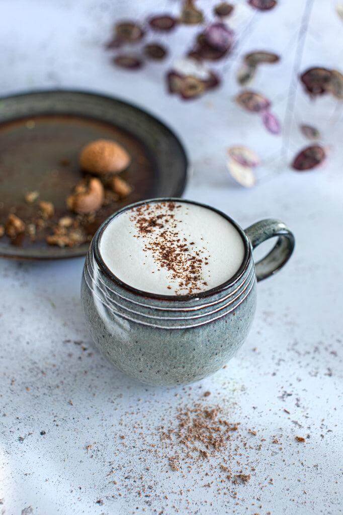 De Comporta Espresso Kopje in aardewerk met schuim, achtergrond van droog fruit voor een stijlvolle tafelsetting.