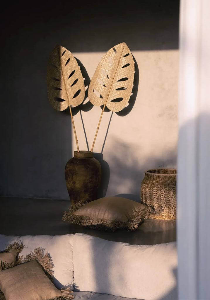 Rustieke woonkamer met jute kussenhoes en decoratieve bladeren in vaas, sfeervol belicht met zonlicht door het raam.