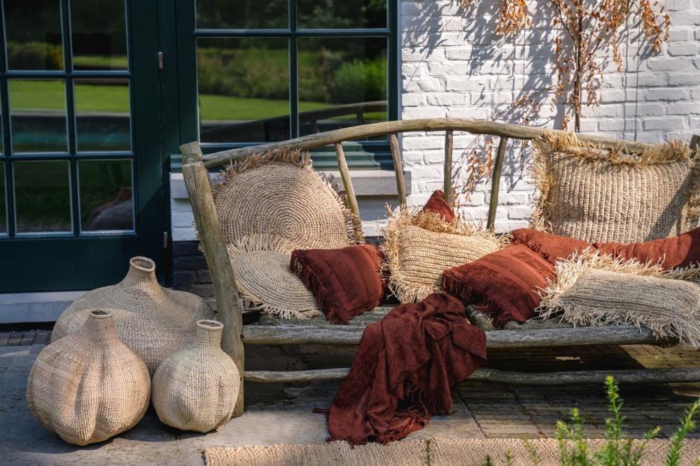 Rustieke tuinbank met boho Bordeaux Velvet kussenhoes en geweven manden voor een gezellige buitenruimte.