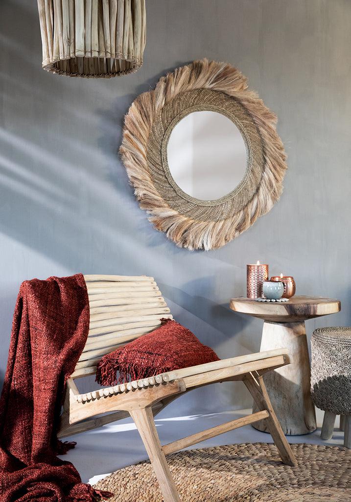 Boho interieur met kersenrode kussenhoes op houten stoel, natuurlijk decor en hangspiegel. Perfect voor een stijlvolle en gezellige sfeer.