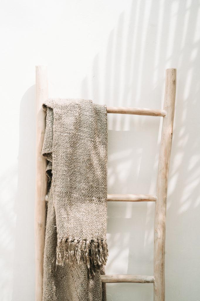 Alt Tag: Luxe handgeweven katoenen plaid beige met franjes op houten ladder, perfect voor gezellige en warme sfeer in elk interieur.