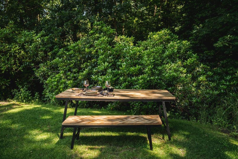 Teakhouten visgraat bank en tafel in natuurlijk licht op grasveld, ideaal voor eettafel binnen en buiten. Inklapbaar ontwerp.