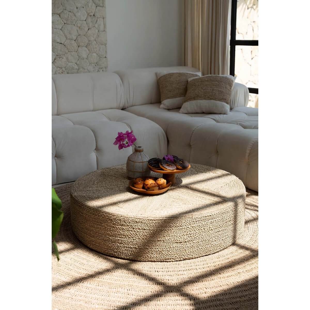 Stijlvolle zeegras poef in een zonnige woonkamer, ideaal voor bohemian interieurs, met decoratieve schalen en bloemen.