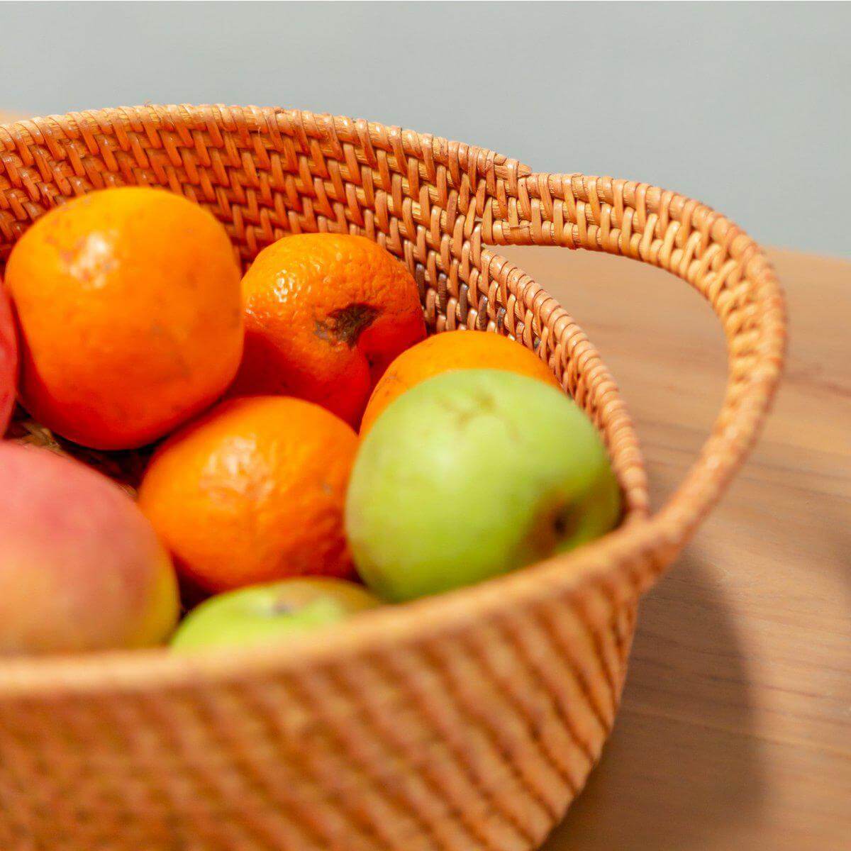 Stijlvolle Suwari mand van rotan met kleurrijk fruit op houten tafel, perfecte broodmand en fruitschaal. Duurzaam en handgemaakt.