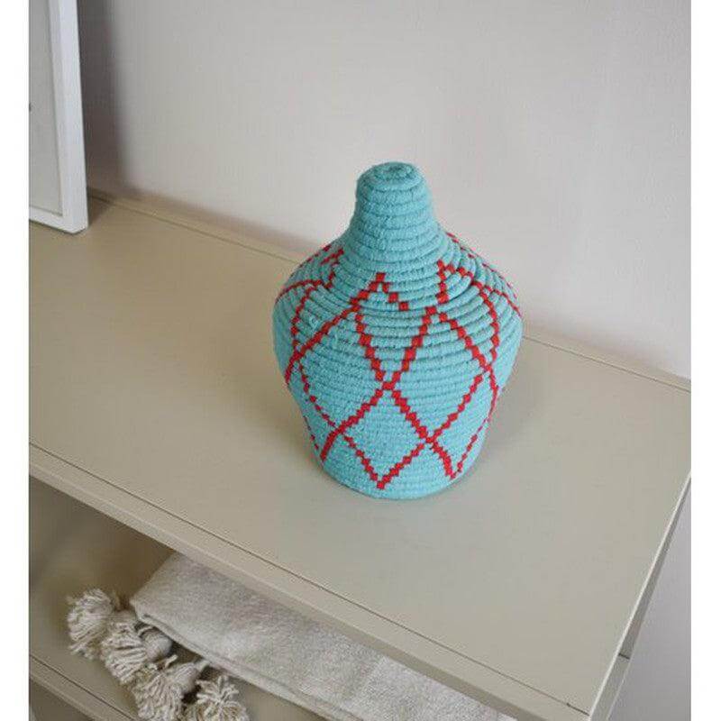 Marokkaanse mand Leila met deksel, handgemaakt van natuurlijke materialen, in turquoise en rood op een beige plank.