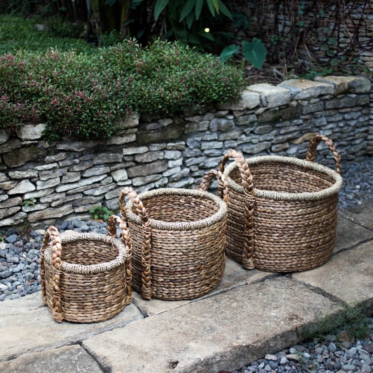 Drie opbergmanden CANGGU van waterhyacint in verschillende maten, met handvatten, geschikt voor planten of als wasmand, op stenen pad.