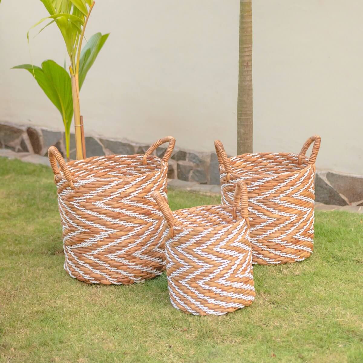 Drie ronde Yalimo manden van waterhyacint in natuur en wit, met handvatten, op een grasveld. Maten: 30, 35 en 40 cm diameter.