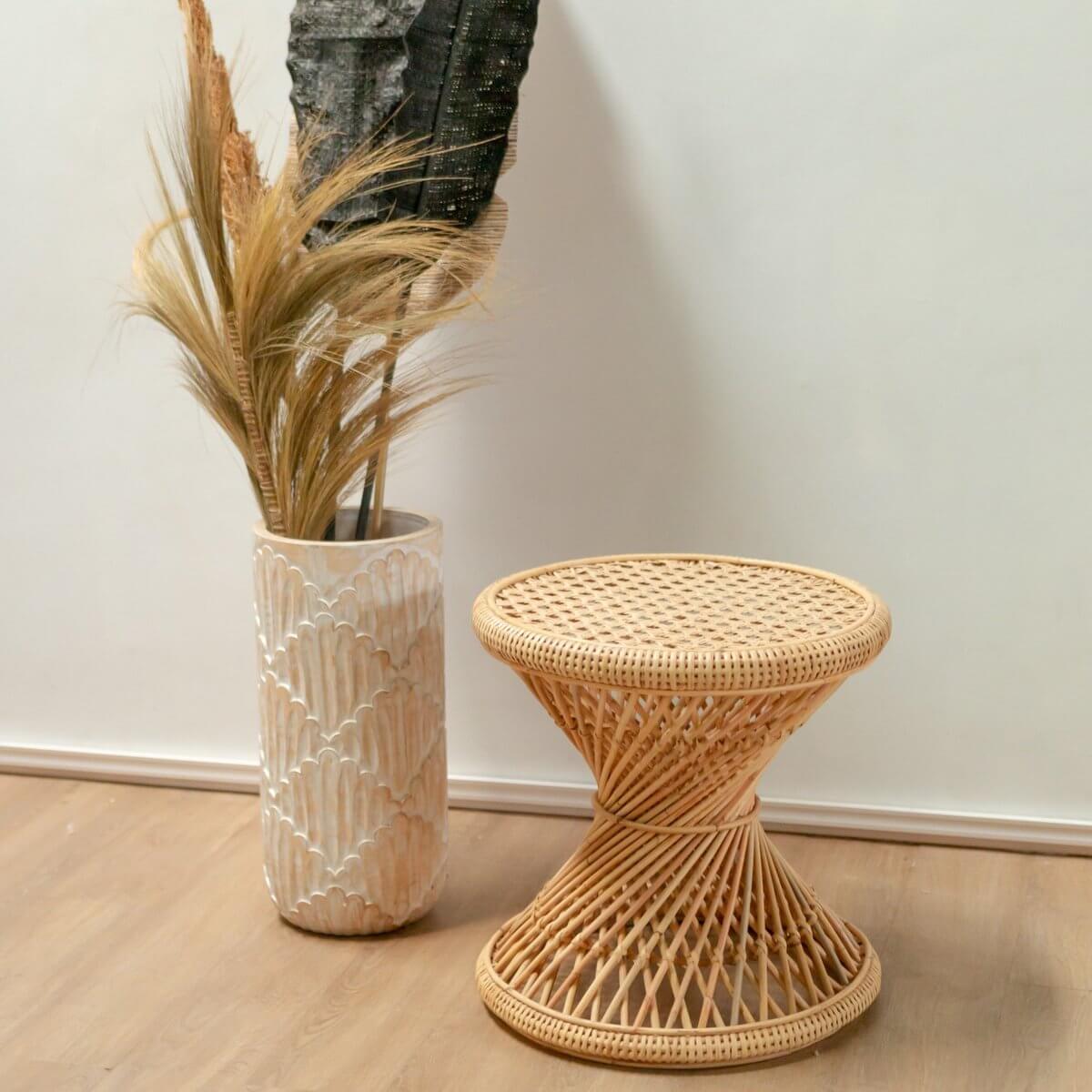 Rotan bijzettafel LUHU Ø45 cm in beige, handgemaakt en duurzaam, naast een decoratieve vaas met pluimen op houten vloer.