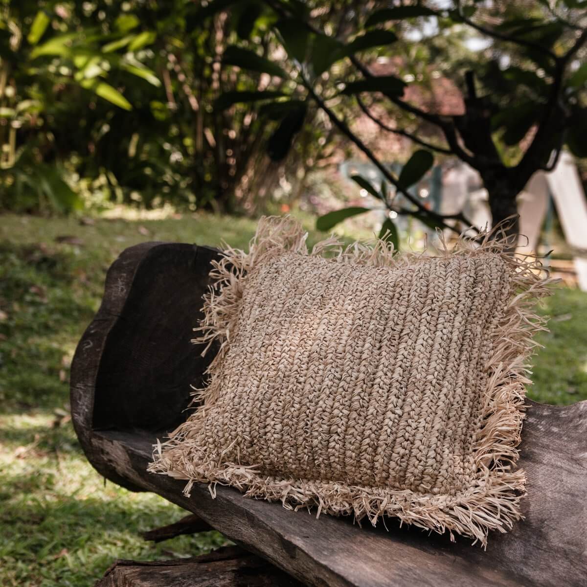 Decoratief kussen van raffia op rustieke houten bank in tuin, handgemaakt en milieuvriendelijk, ideaal voor bed of bank.